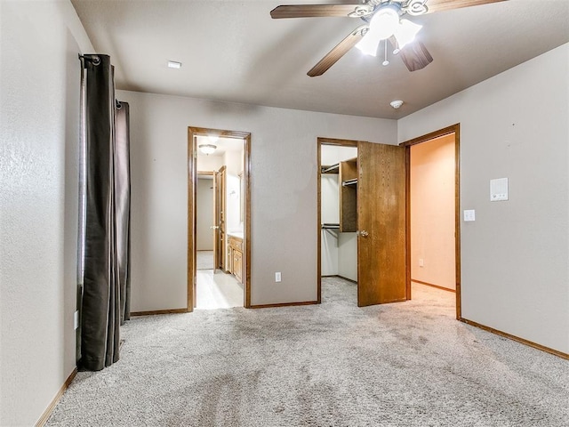 unfurnished bedroom featuring light carpet, a walk in closet, ensuite bathroom, ceiling fan, and a closet