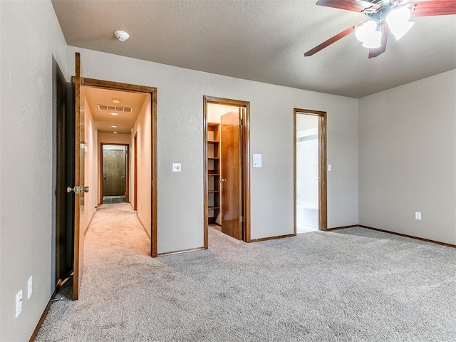 unfurnished bedroom featuring a walk in closet, ensuite bath, ceiling fan, light colored carpet, and a closet