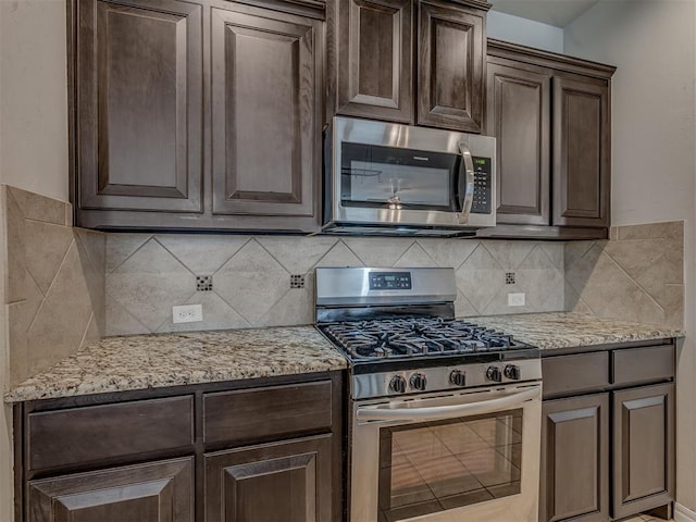 kitchen featuring decorative backsplash, dark brown cabinets, light stone countertops, and appliances with stainless steel finishes