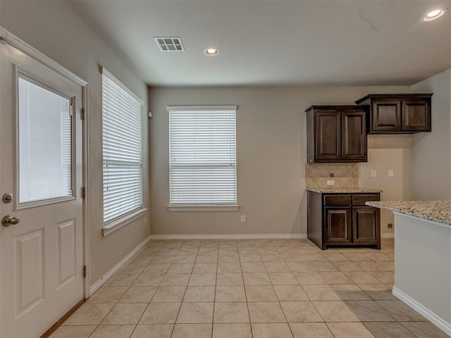 kitchen featuring dark brown cabinets, light tile patterned flooring, light stone counters, and backsplash