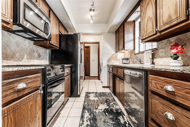 kitchen with backsplash, track lighting, light tile patterned floors, light stone countertops, and appliances with stainless steel finishes