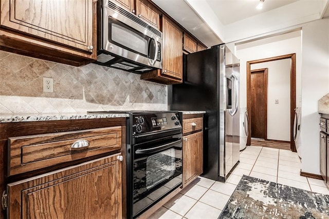 kitchen featuring dark stone counters, light tile patterned floors, tasteful backsplash, stacked washer / drying machine, and stainless steel appliances