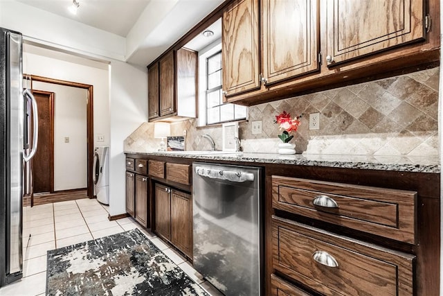 kitchen with decorative backsplash, appliances with stainless steel finishes, light stone counters, light tile patterned floors, and independent washer and dryer