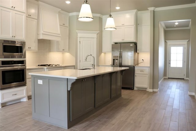 kitchen with white cabinetry, stainless steel appliances, an island with sink, pendant lighting, and custom exhaust hood