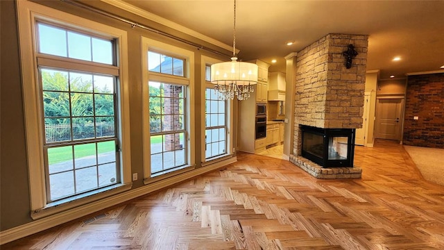 unfurnished living room with a chandelier, a healthy amount of sunlight, a stone fireplace, and light parquet floors