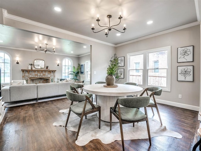 dining room featuring a chandelier, a stone fireplace, crown molding, and dark wood-type flooring