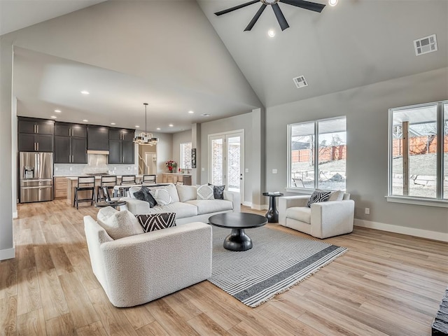 living room featuring light wood-type flooring, ceiling fan with notable chandelier, and high vaulted ceiling