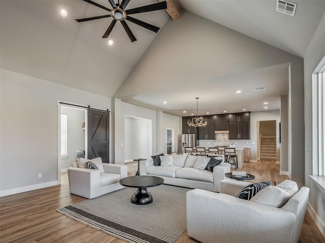 living room with beam ceiling, a barn door, high vaulted ceiling, light hardwood / wood-style floors, and ceiling fan with notable chandelier