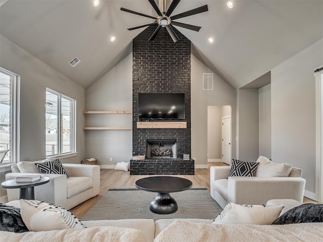 living room with ceiling fan, light wood-type flooring, lofted ceiling, and a brick fireplace