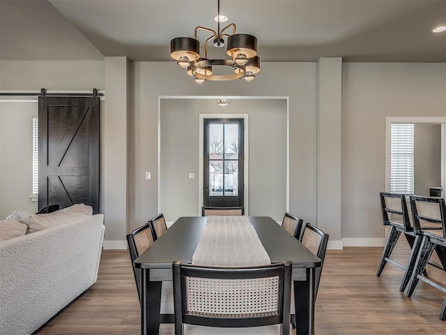 dining space featuring a barn door, light hardwood / wood-style flooring, plenty of natural light, and a notable chandelier