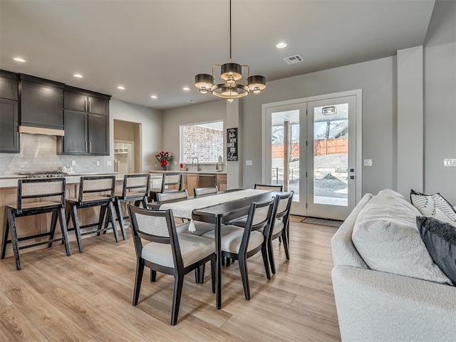 dining area with light wood-type flooring, sink, and an inviting chandelier