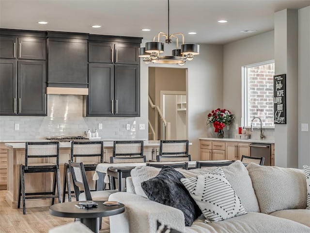 kitchen with sink, ventilation hood, backsplash, a chandelier, and decorative light fixtures