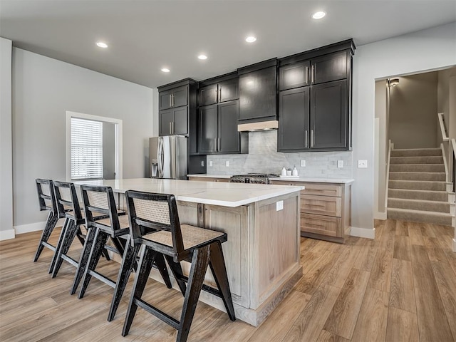 kitchen featuring a kitchen bar, tasteful backsplash, light hardwood / wood-style flooring, stainless steel fridge with ice dispenser, and a kitchen island