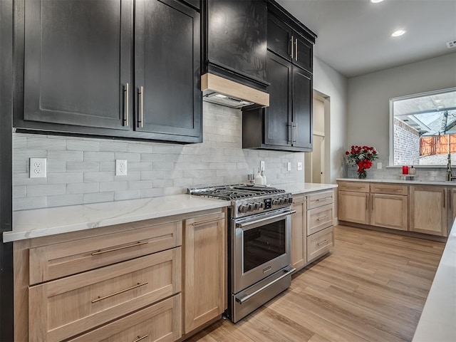 kitchen with decorative backsplash, light brown cabinetry, stainless steel range, light hardwood / wood-style floors, and light stone counters