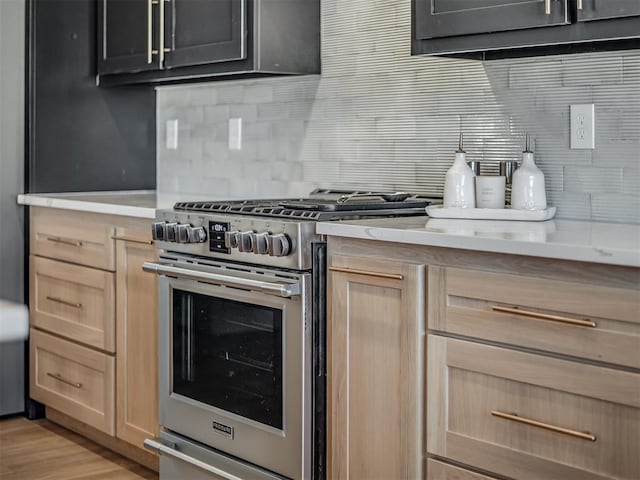 kitchen with decorative backsplash, light brown cabinetry, and high end stove