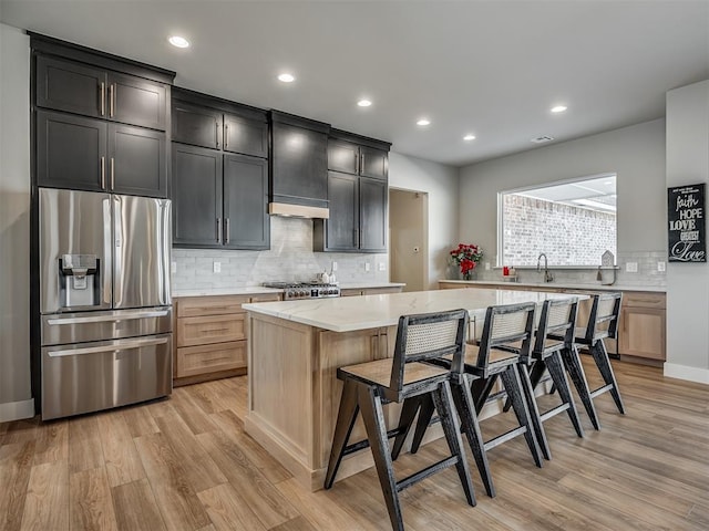 kitchen with a kitchen breakfast bar, light hardwood / wood-style floors, a kitchen island, light stone counters, and stainless steel appliances