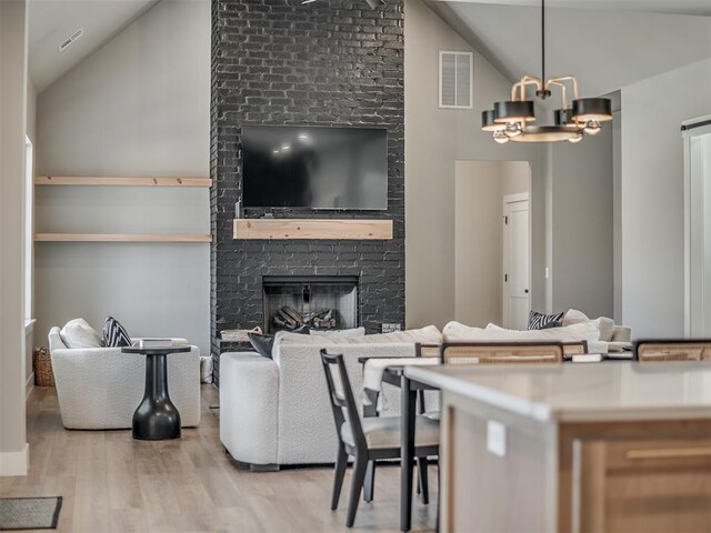 living room featuring a fireplace, light wood-type flooring, lofted ceiling, and an inviting chandelier