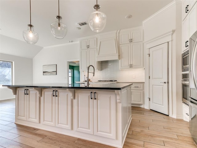 kitchen featuring white cabinetry, custom exhaust hood, a kitchen island with sink, and decorative light fixtures