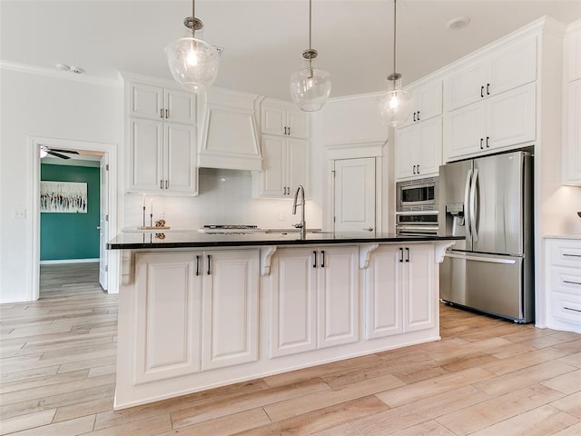 kitchen with appliances with stainless steel finishes, a center island with sink, white cabinets, decorative light fixtures, and ornamental molding