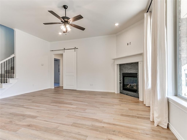 unfurnished living room featuring ceiling fan, a barn door, ornamental molding, and light hardwood / wood-style flooring