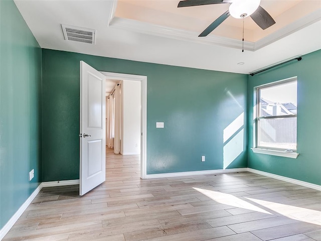 empty room featuring a tray ceiling, ceiling fan, and light hardwood / wood-style floors