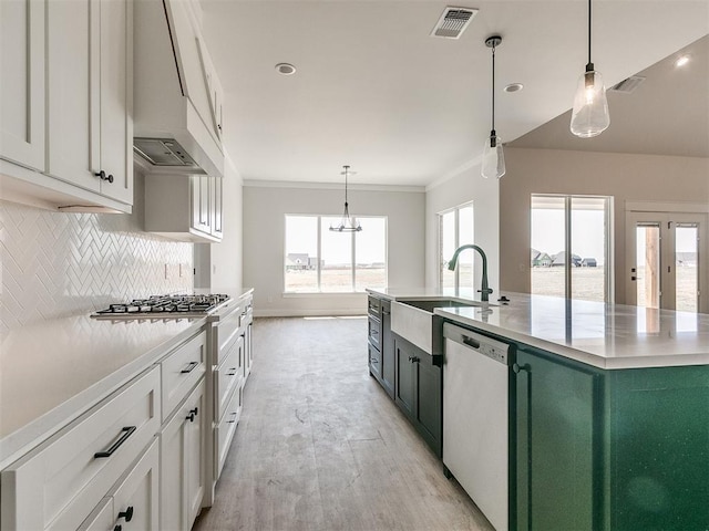 kitchen with a center island with sink, white cabinetry, stainless steel appliances, and hanging light fixtures