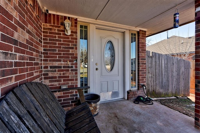 property entrance with fence, covered porch, and brick siding