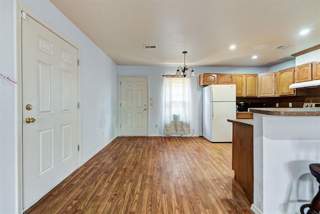 kitchen featuring visible vents, freestanding refrigerator, under cabinet range hood, and an inviting chandelier