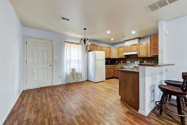 kitchen featuring electric range, freestanding refrigerator, a peninsula, under cabinet range hood, and visible vents