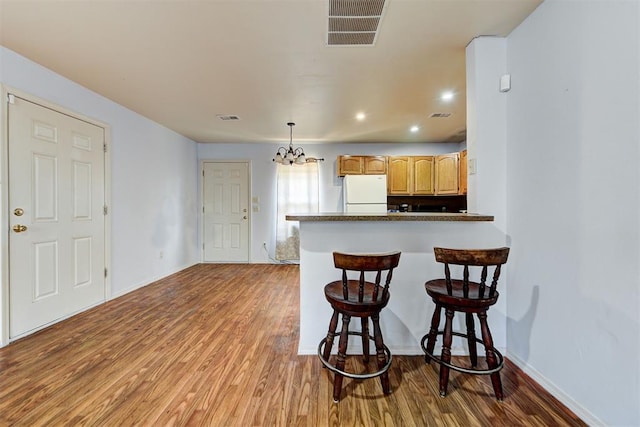 kitchen featuring freestanding refrigerator, visible vents, wood finished floors, and a kitchen bar
