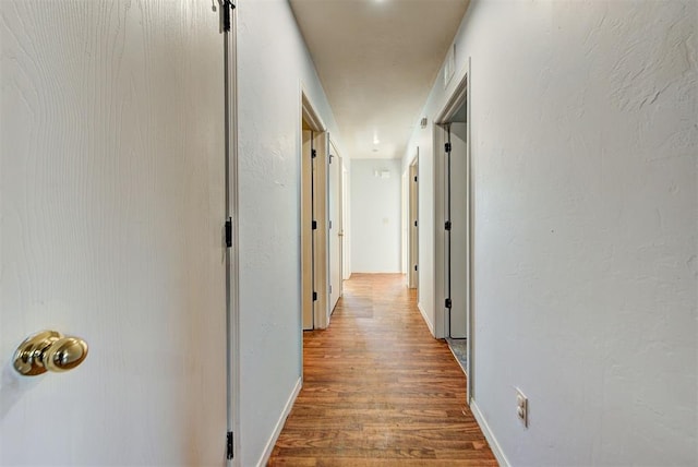 hallway featuring baseboards, visible vents, and wood finished floors