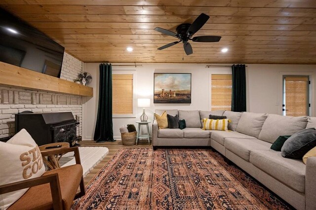 living room with hardwood / wood-style flooring, ceiling fan, a wood stove, and wooden ceiling