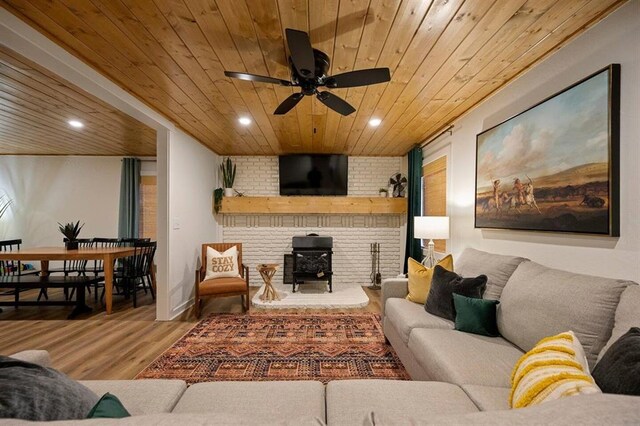 living room with a wood stove, ceiling fan, wooden ceiling, brick wall, and hardwood / wood-style floors