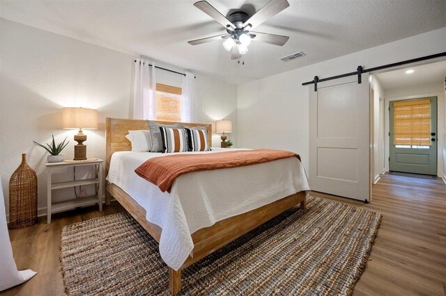 bedroom featuring a barn door, ceiling fan, and dark hardwood / wood-style floors