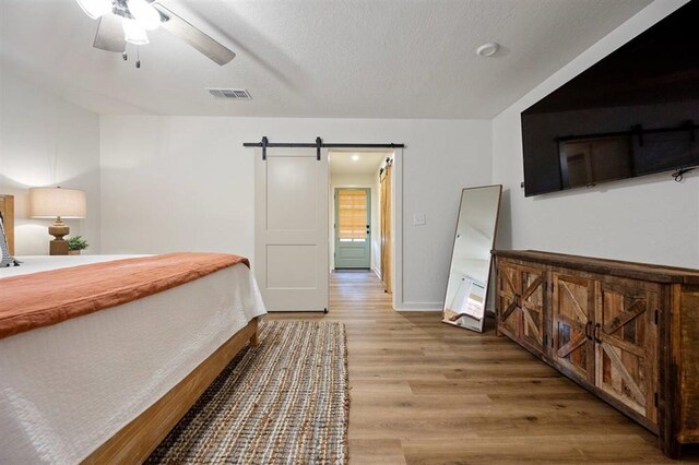 bedroom featuring wood-type flooring, a barn door, and ceiling fan