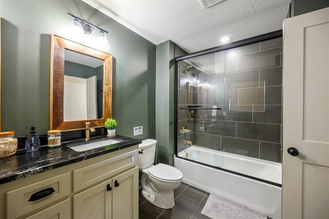 full bathroom with tile patterned flooring, bath / shower combo with glass door, a textured ceiling, toilet, and vanity