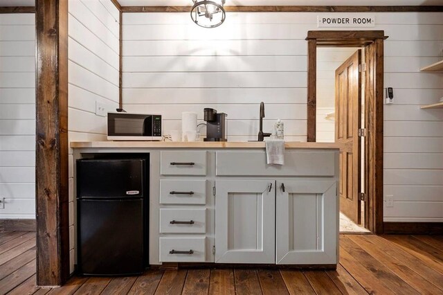 bar featuring black refrigerator, dark hardwood / wood-style floors, and wooden walls