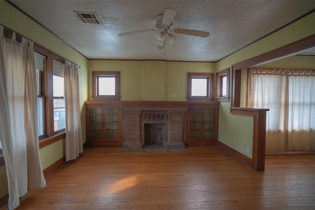 unfurnished living room featuring ceiling fan, wood-type flooring, a textured ceiling, and a brick fireplace