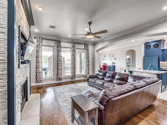 living room with a textured ceiling, a fireplace, ceiling fan, ornamental molding, and hardwood / wood-style flooring