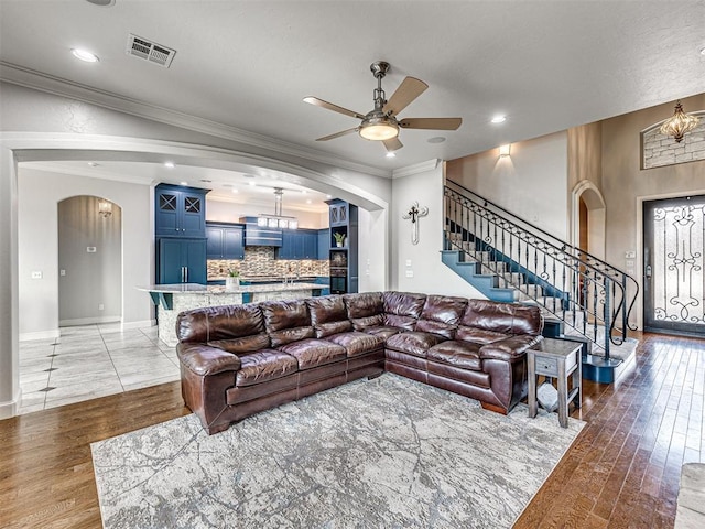 living room with crown molding, dark wood-type flooring, and ceiling fan with notable chandelier