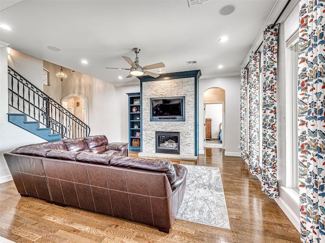 living room with ceiling fan, wood-type flooring, ornamental molding, and a fireplace