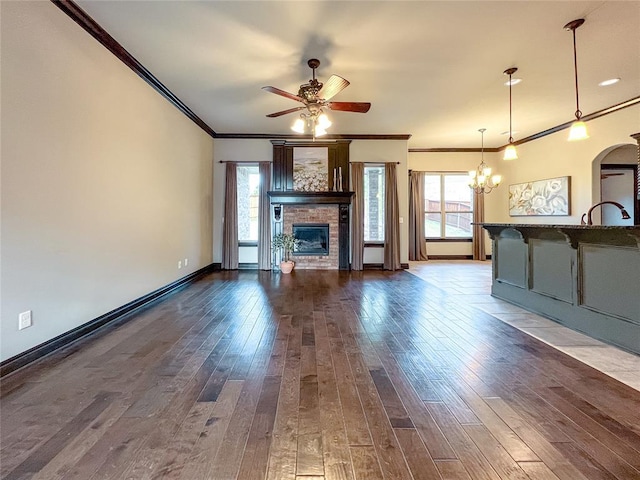 unfurnished living room featuring hardwood / wood-style floors, ceiling fan with notable chandelier, a stone fireplace, and crown molding