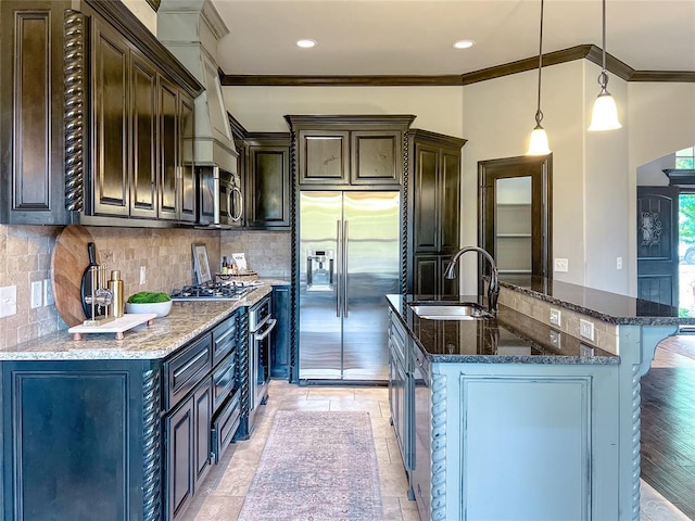 kitchen featuring dark brown cabinetry, sink, hanging light fixtures, stainless steel appliances, and a center island with sink