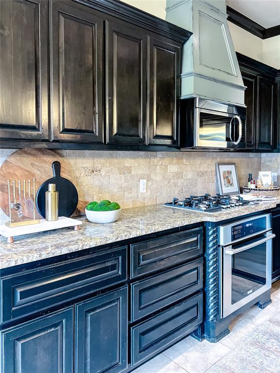 kitchen featuring light tile patterned floors, ornamental molding, appliances with stainless steel finishes, tasteful backsplash, and light stone counters