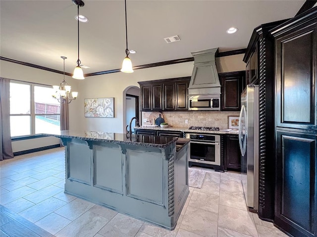 kitchen with tasteful backsplash, an island with sink, pendant lighting, appliances with stainless steel finishes, and ornamental molding