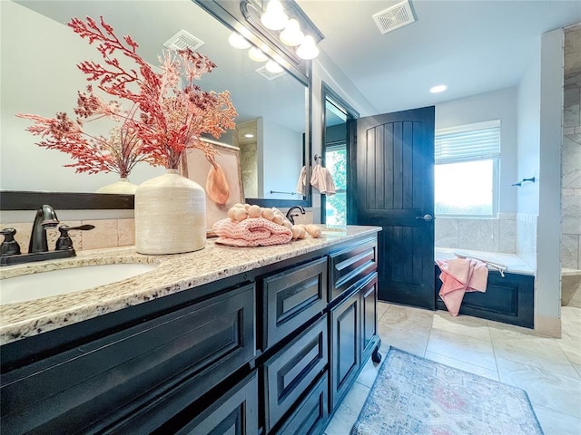 bathroom with tile patterned floors, vanity, and tiled bath