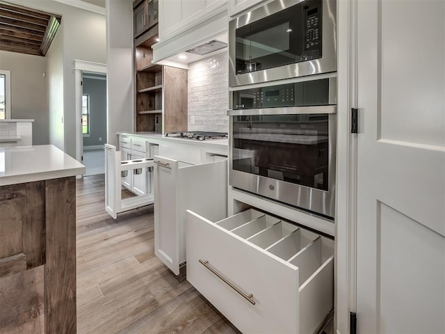 kitchen featuring stainless steel gas stovetop, light wood-style flooring, white cabinets, and built in microwave