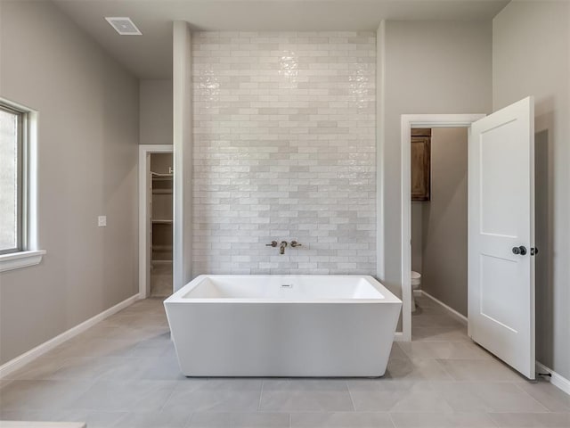 bathroom featuring visible vents, toilet, a freestanding tub, baseboards, and tile patterned floors