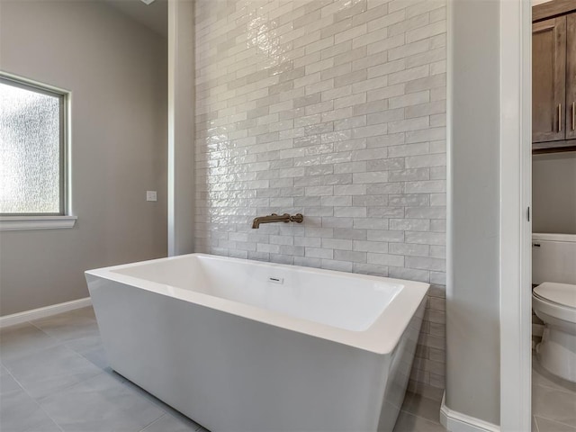 full bath featuring tile patterned flooring, baseboards, a freestanding bath, and toilet