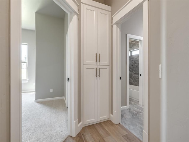 corridor with baseboards and light colored carpet